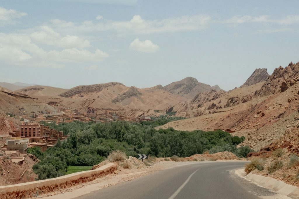 Winding road through arid desert landscape with greenery.